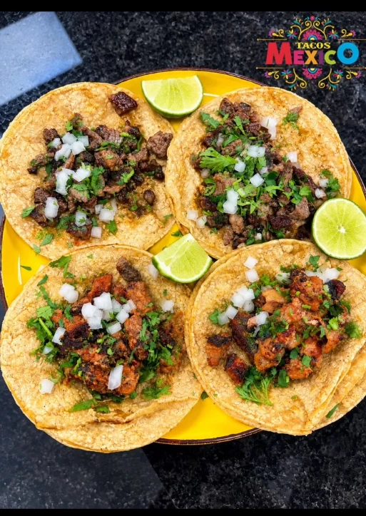 Four Mexican tacos topped with onions and cilantro, served with lime
